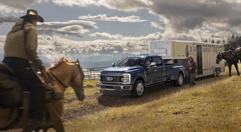 A blue 2023 Ford F-250 Super Duty is shown parked off-road while towing a horse trailer.