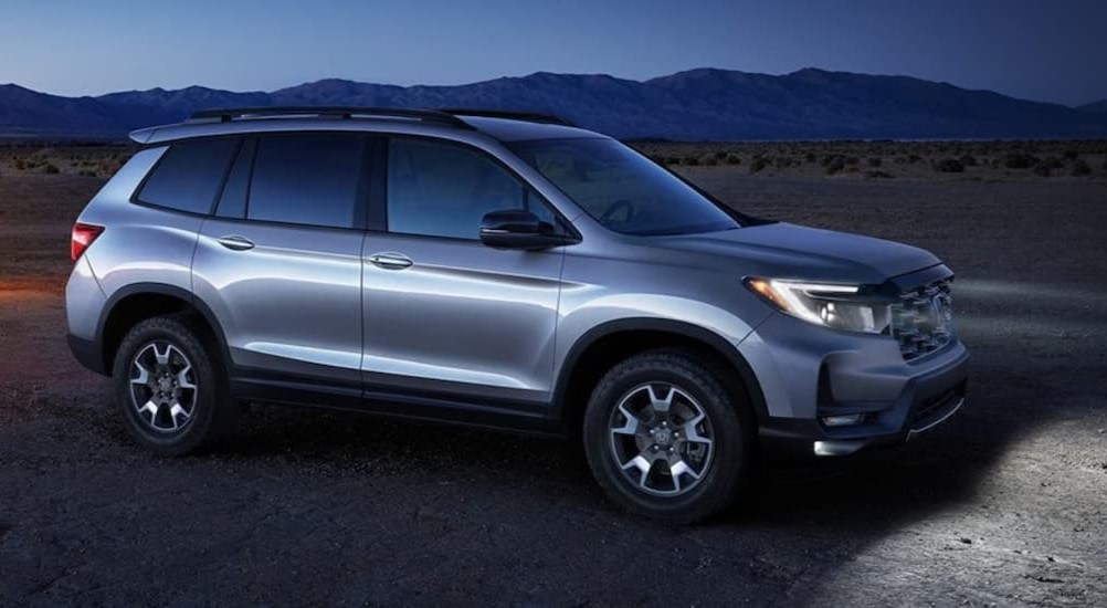 A silver 2023 Honda Passport is shown parked off-road in the dark.