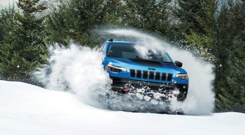 Fresh from a Jeep dealer, a blue 2023 Jeep Cherokee Trailhawk is shown plowing through snow.