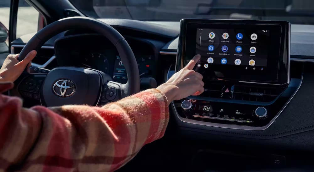 A person is shown touching the dashboard screen in the interior of a 2023 Toyota Corolla.
