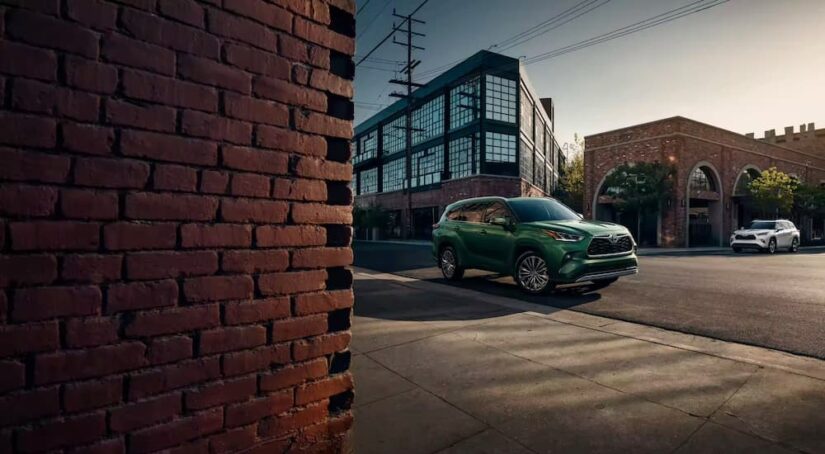 A green 2023 Toyota Highlander Hybrid for sale is shown parked near a brick wall.