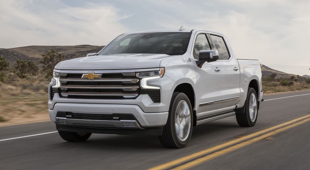 A white 2024 Chevy Silverado 1500 HD High Country is shown driving on a highway.
