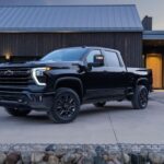 A black 2024 Chevy Silverado 2500 HD High Country is shown parked near a Chevy dealer.