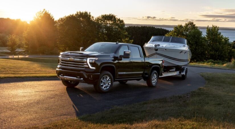 A black 2024 Chevy Silverado 2500 HD High Country is shown towing a boat through the countryside after visiting a Chevy dealer.