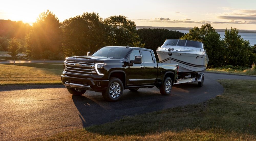 A black 2024 Chevy Silverado 2500 HD High Country is shown towing a boat through the countryside.