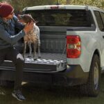 The tailgate of a gray 2024 Ford Maverick is shown with a person and a dog sitting on it.