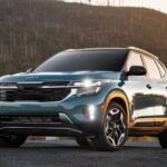 A trim of the Kia Seltos for sale, a blue 2024 Kia Seltos S is shown driving during a sunset, with a mountain in the background.