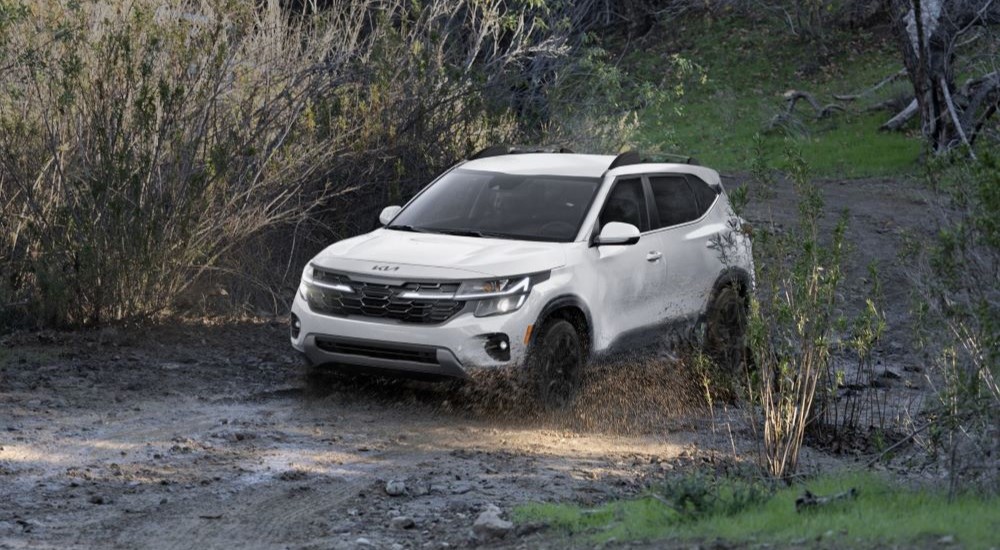 A white 2024 Kia Seltos is shown driving on a muddy road.