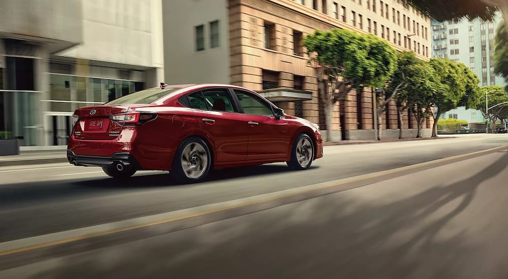 A red 2024 Subaru Legacy is shown driving on a city street.
