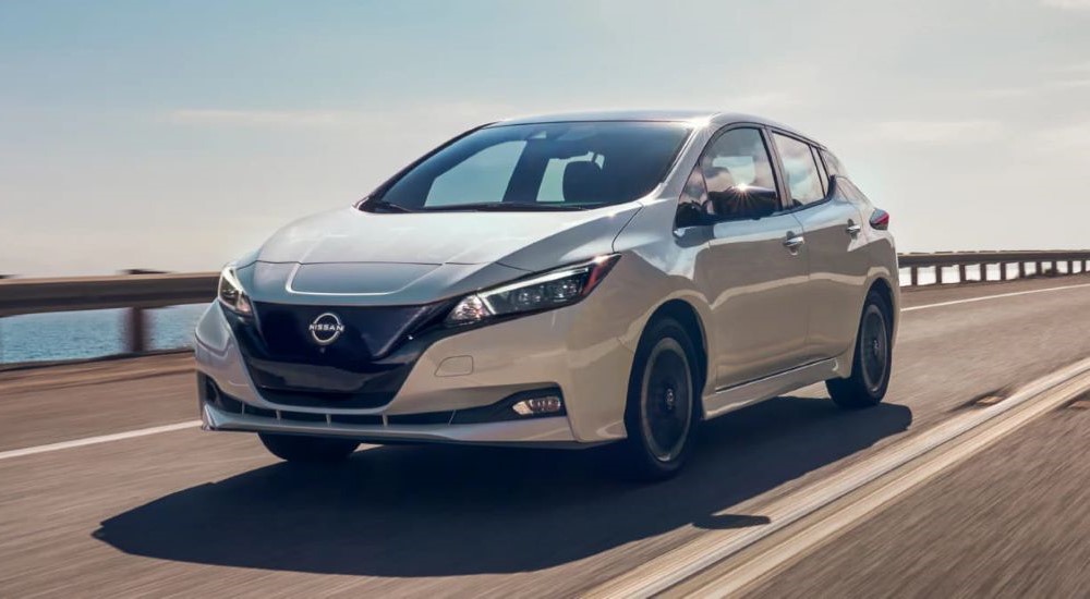 A white 2023 Nissan LEAF is shown driving on a bridge.