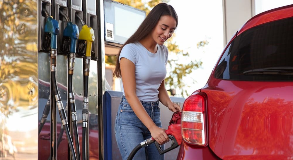 A person is shown pumping gas into a red car.
