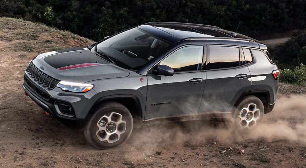 A black 2023 Jeep Compass is shown driving over a dusty dirt road.