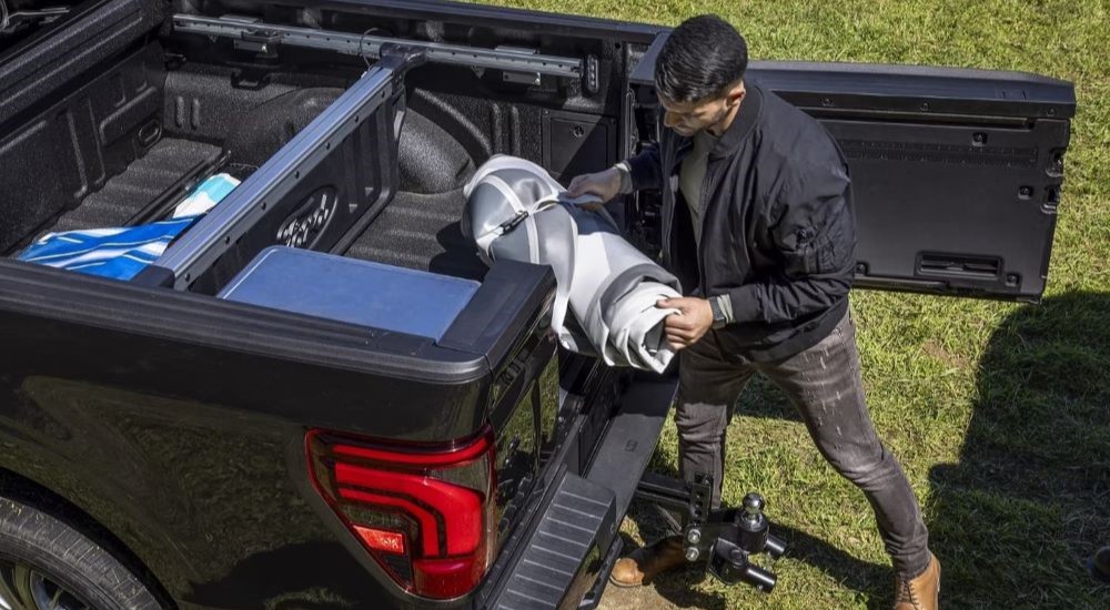 A person is shown stowing gear on the bed of a black 2024 Ford F-150.