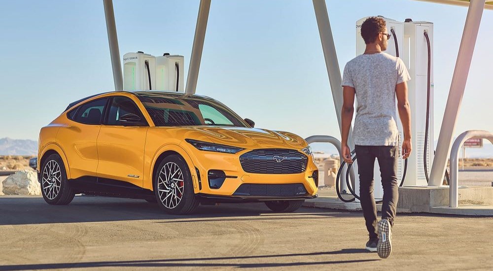 A person is shown walking near a charging yellow 2023 Ford Mustang Mach-E GT.
