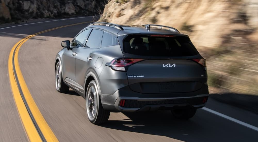 A gray 2023 Kia Sportage PHEV is shown from the rear driving on a highway.