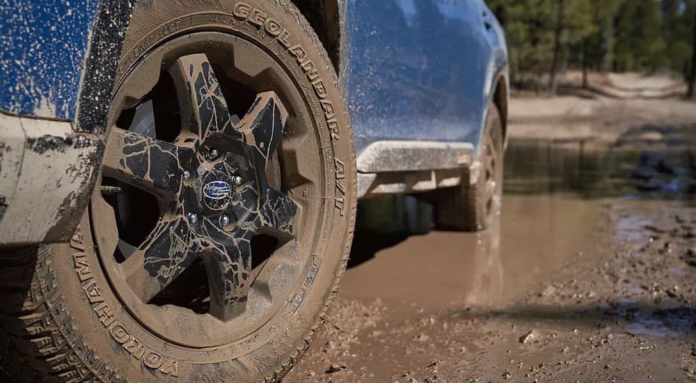 A close-up on the muddy wheel of a blue 2023 Subaru Outback Wilderness is shown.