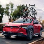 A black and red 2023 Subaru Solterra for sale is shown driving on a city road.