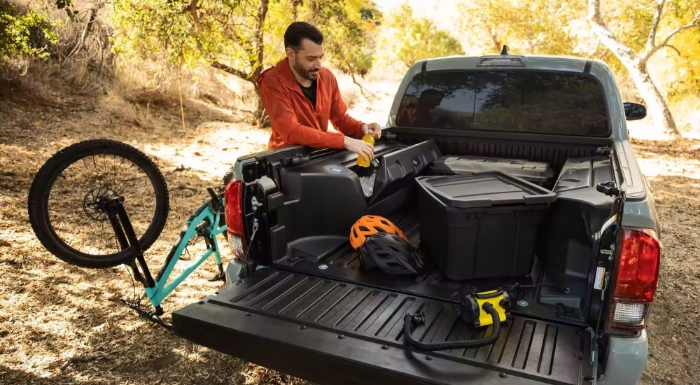 A person is shown offloading a bike from the bed of a black 2023 Toyota Tacoma SR5 Trail Edition.