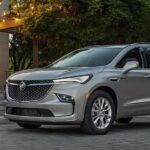 Two people are shown walking near a silver 2024 Buick Enclave Avenir.
