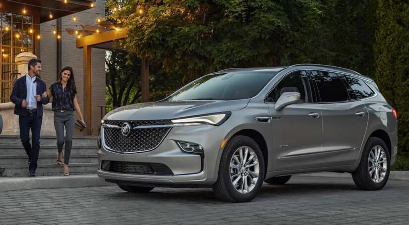Two people are shown walking near a silver 2024 Buick Enclave Avenir.