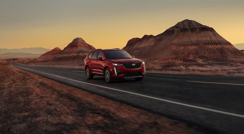 A red 2024 Cadillac XT6 is shown driving on a highway.
