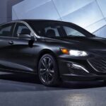 A black 2024 Chevy Malibu Midnight is shown parked in a garage.