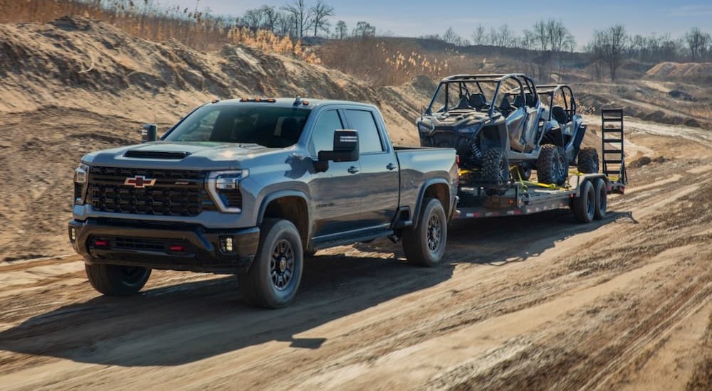 A gray 2024 Chevy Silverado 2500HD ZR2 High Country is shown towing a trailer off-road.