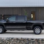 A black 2024 Chevy Silverado 3500HD High Country is shown parked near a house after visiting a Chevy dealer.