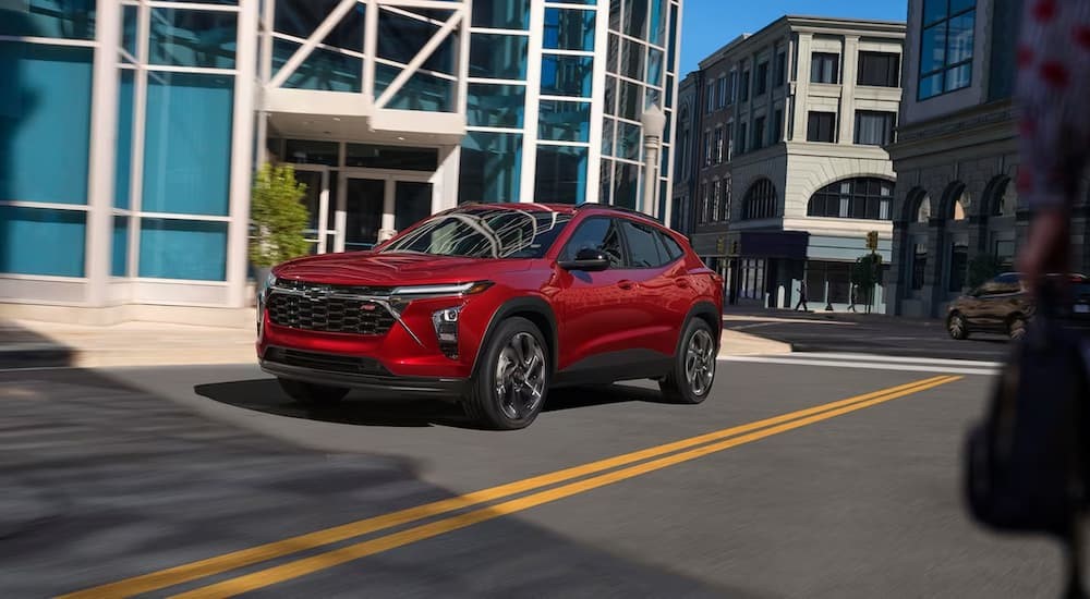 A red 2024 Chevy Trax RS is shown driving on a city street.