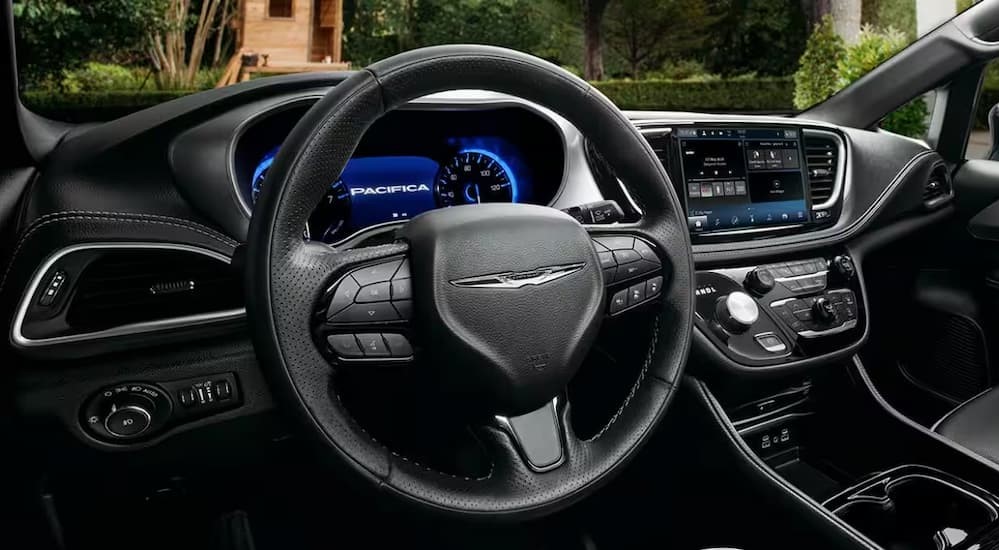The black interior of a 2024 Chrysler Pacifica is shown, including the wheel and dashboard.