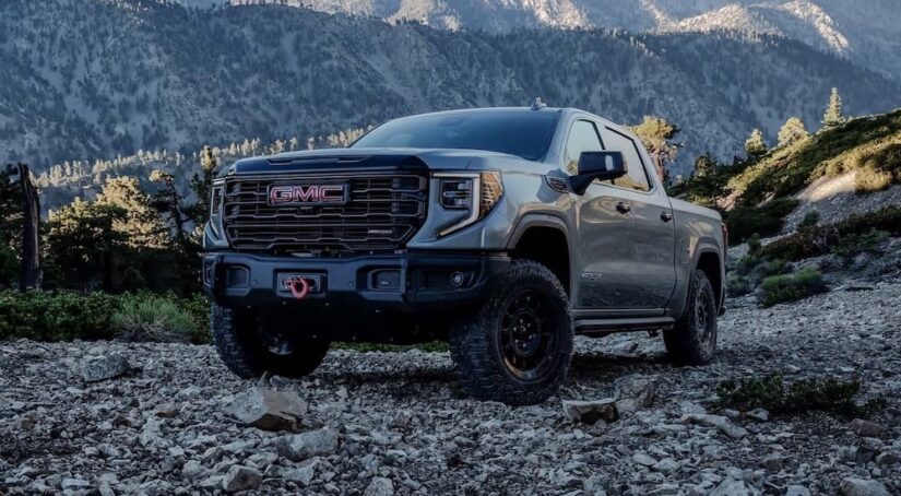 The newest GMC Sierra for sale, a grey 2024 GMC Sierra 1500 AT4X, is shown driving off-road in the mountains.