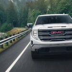 A white 2024 GMC Sierra 1500 Pro is shown driving on a highway near a river after viewing GMC trucks for sale.