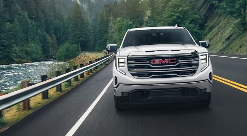 A white 2024 GMC Sierra 1500 Pro is shown driving on a highway near a river after viewing GMC trucks for sale.