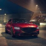 A red 2024 Genesis G70 is shown parked in a city at night.
