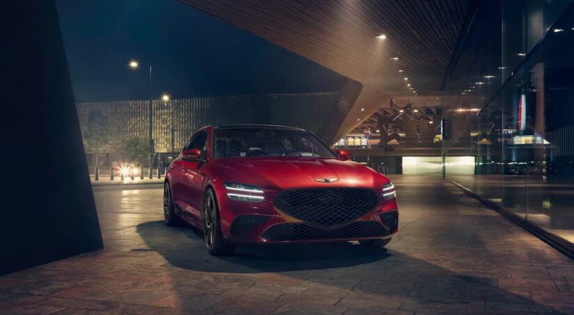 A red 2024 Genesis G70 is shown parked in a city at night.