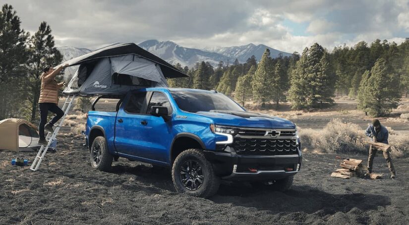 A blue 2023 Chevy Silverado 1500 ZR2 is shown parked at a campsite with a pop-up tent set up in the bed.