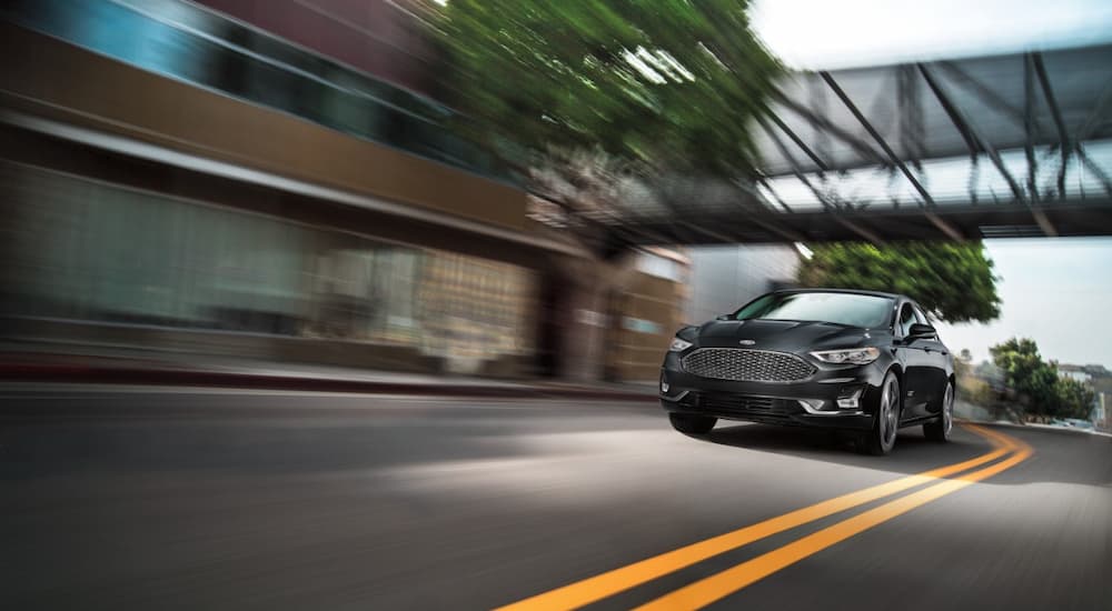 A black 2020 Ford Fusion Energi Titanium is shown driving on a city street.