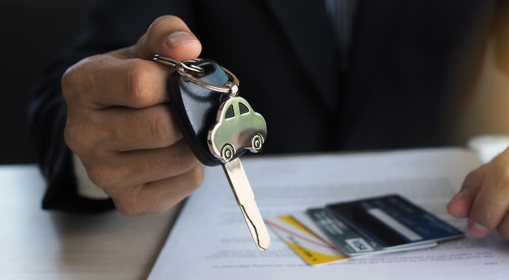 A close up of a set of car keys are shown with paperwork at a used car dealer.