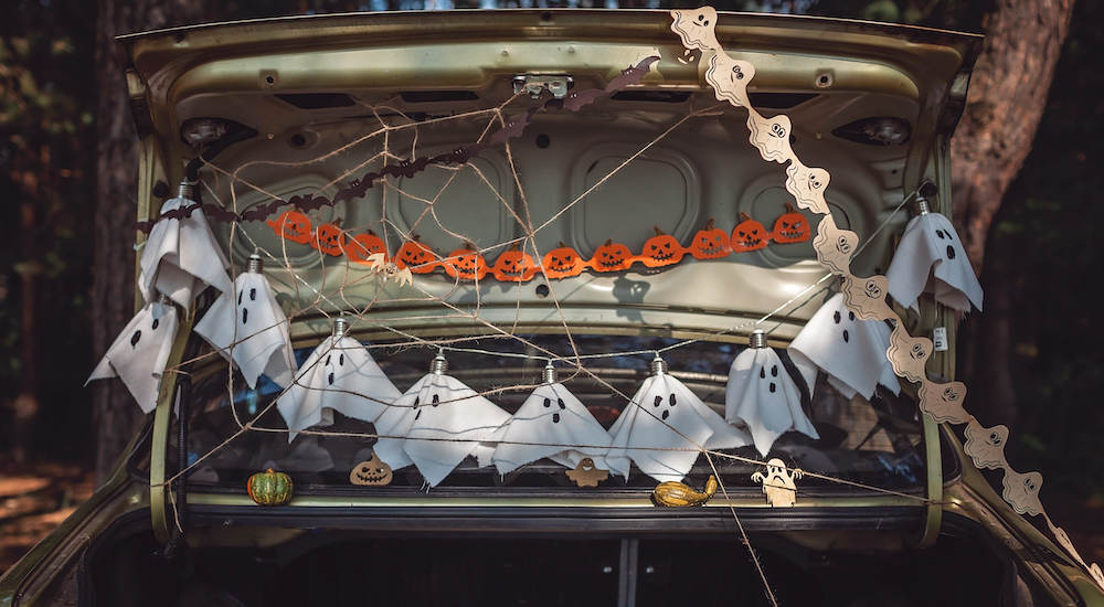 An open car trunk is shown decorated with various halloween decorations, including wireframe spider webs and hanging ghosts.
