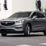A silver 2021 Buick Enclave is shown driving from a used Buick dealership.