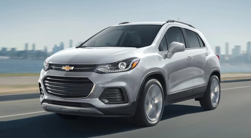 A silver 2021 Chevy Trax is shown driving away from a used Chevy dealer.
