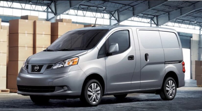 One of many popular used vans for sale, a silver 2021 Nissan NV200, is shown parked next to boxes.