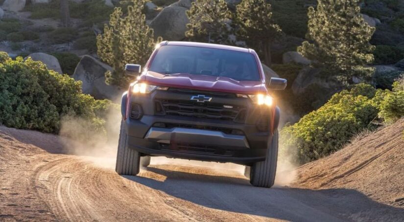 A red 2023 Chevy Colorado for sale is shown with the Trail Boss trim, driving down a dirt road.