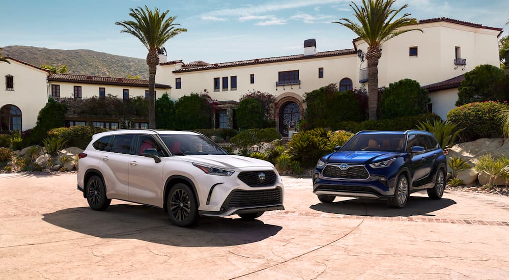 A white 2023 Toyota Highlander XSE Hybrid and a blue 2023 Toyota Highlander Platinum are shown parked together near a house.