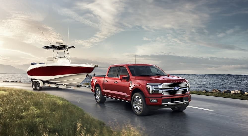 A red 2024 Ford F-150 is shown towing a boat near a lake.