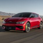 A red 2024 Kia EV6 is shown driving on a curved road.