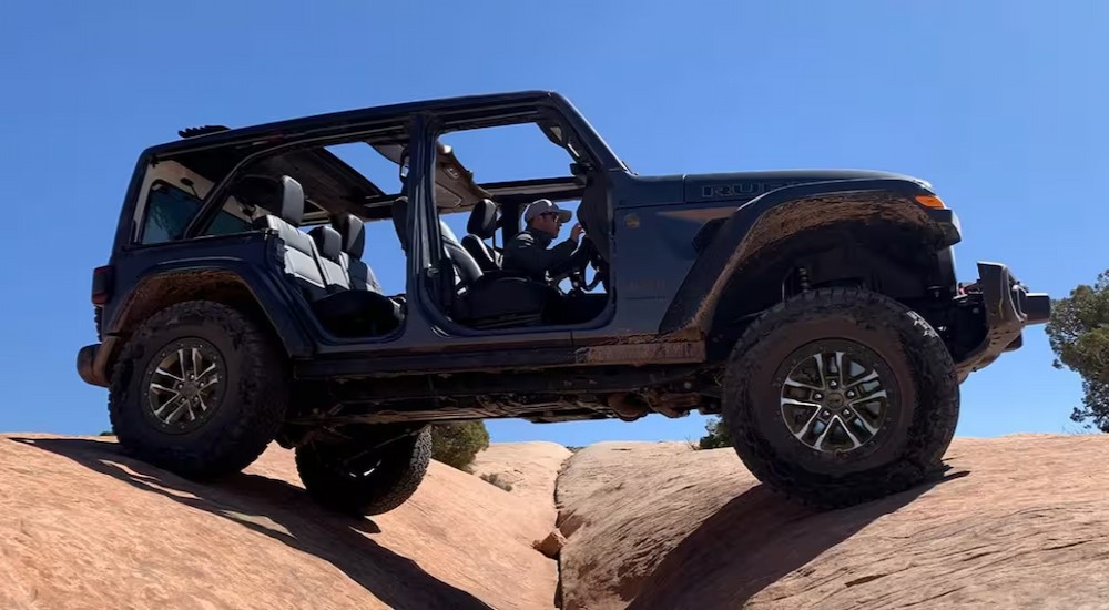 A blue 2024 Jeep Wrangler 4xe Rubicon is shown parked on two boulders after viewing a Jeep Wrangler 4xe for sale.