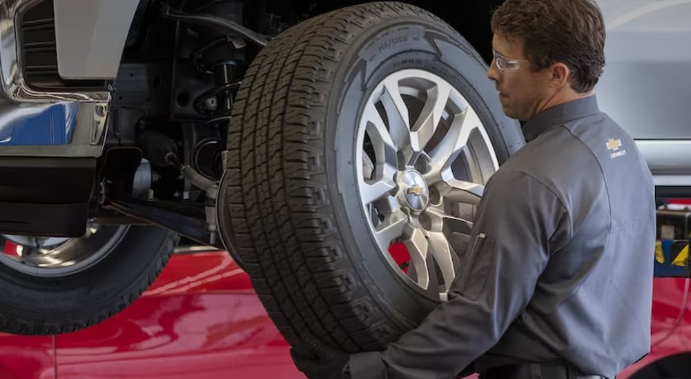 A mechanic at a used car dealership is shown putting a tire on a vehicle.