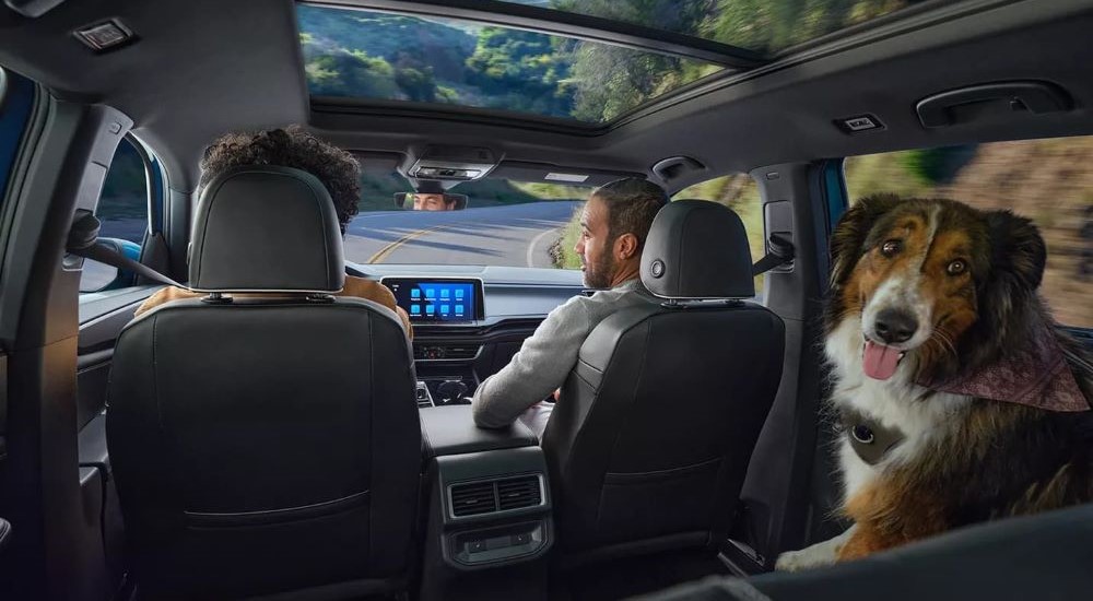 People and a dog are shown in a 2024 Volkswagen Atlas Cross Sport driving on an open road.