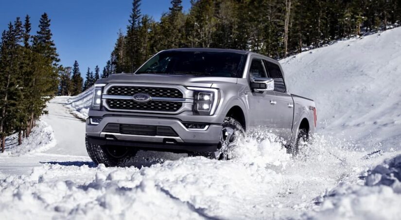 One of the most popular used trucks for sale, a silver 2023 Ford F-150, is shown driving through snow.